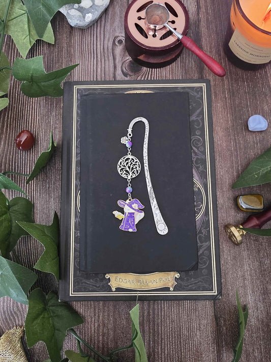 Un marque-page en métal inspiré de la fantasy et de la sorcellerie, orné d’un petit chat sorcier plongé dans son grimoire et de pierres naturelles personnalisables : jaspe violet sur le modèle.