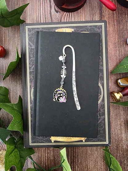 Ce marque-page en métal argenté est orné d'un petit chat noir sorcier, installé devant sa boule de cristal sous un ciel étoilé. Il est accompagné d'une breloque en forme d'arête de poisson et de véritables pierres naturelles de labradorite noire.