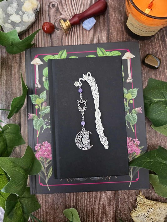 Ce marque-page en métal argenté est orné d'une chouette nichée dans un croissant de lune, accompagnée de délicates arabesques et de véritables pierres naturelles personnalisables : améthyste sur le modèle.