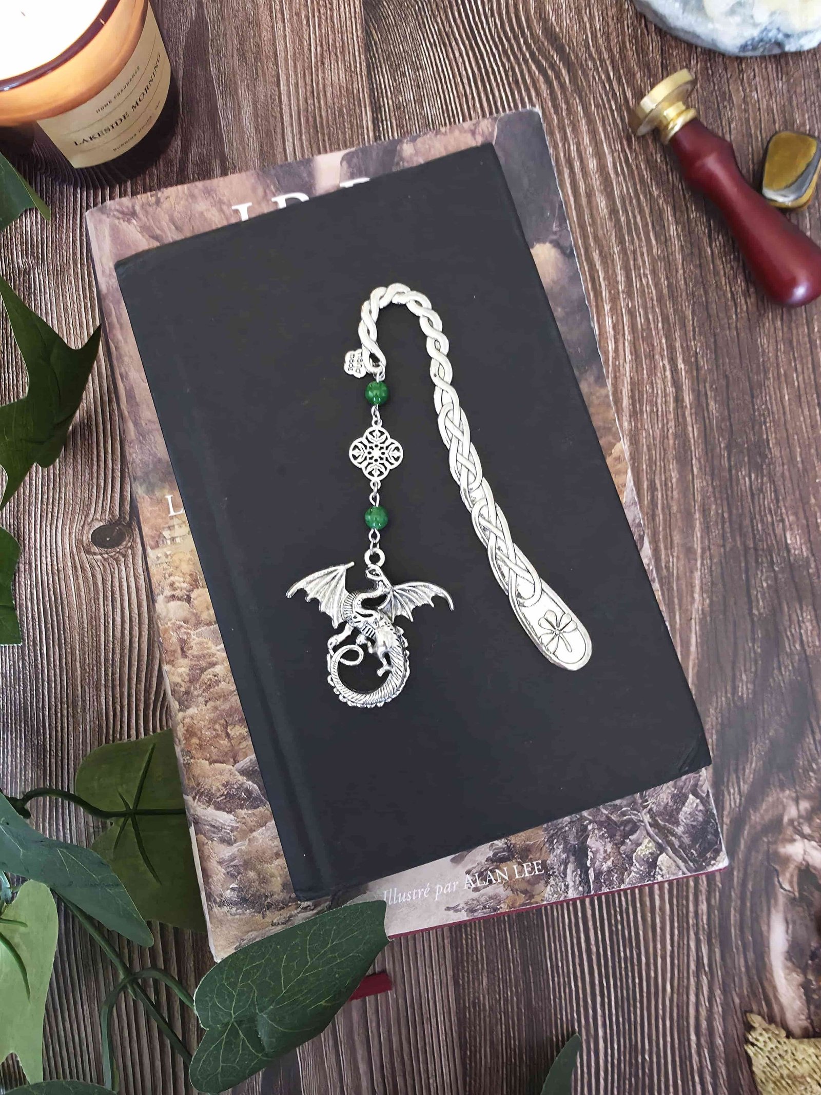 Marque-page en métal Dragon orné de pierres fines naturelles de jade, personnalisable. Le signet est posé sur un livre noir, un livre de Tolkien en dessous. 