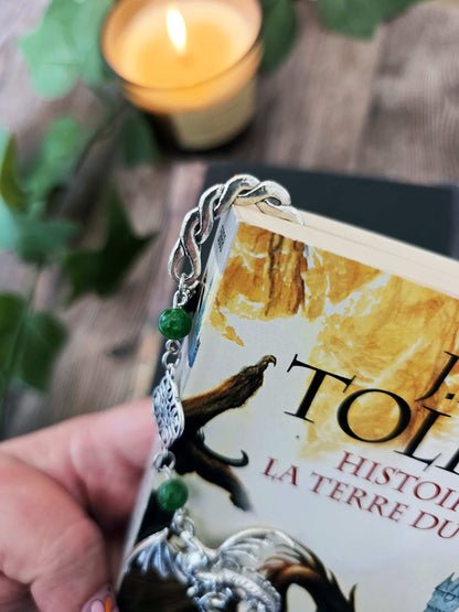 Marque-page en métal Dragon orné de pierres fines naturelles de jade, personnalisable. Le signet est posé sur un livre noir, un livre de Tolkien en dessous. 