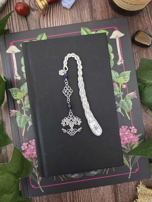 Un marque-page arbre de vie/Yggdrasil en métal. Ses entrelacs délicats et son arbre aux branches nouées évoquent les anciens royaumes elfiques, la nature et les légendes fantastiques et nordiques. Sur le modèle présenté, les perles sont du lapis-lazuli, mais vous pouvez choisir les pierres naturelles qui accompagneront votre marque-page.