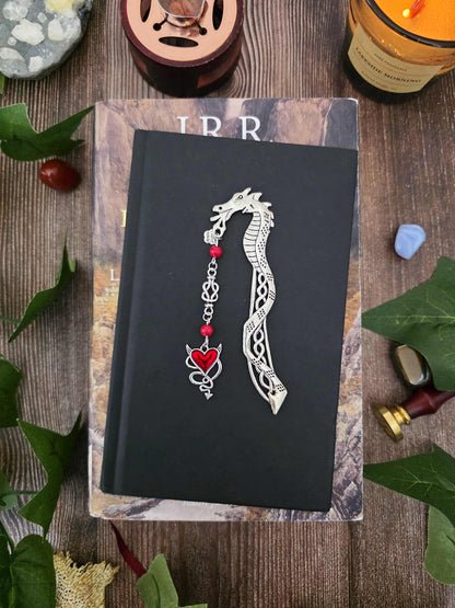 Ce marque-page dragon en métal argenté est orné d’un cœur rouge aux détails entrelacés, accompagné de véritables pierres naturelles : corail rouge sur le modèle.