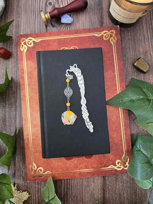 Ce marque-page en métal est orné d’un médaillon représentant Hauru, inspiré du chateau ambulant et de perles en pierres naturelles. Une création artisanale inspirée par la magie et les univers fantasy, pensée pour accompagner vos lectures et apporter une petite touche enchantée à votre bibliothèque.
